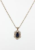 A yellow metal pendant set with an oval faceted cut blue sapphire and suspended from a belcher link