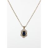 A yellow metal pendant set with an oval faceted cut blue sapphire and suspended from a belcher link