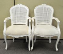 A pair of white painted French style open arm chairs,