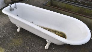 An early 20th century cast iron enamelled roll top bath tub, raised upon four claw and ball feet,