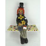 An unusual papier mache figure of a clown perched on a shelf,