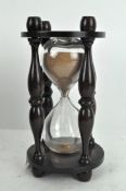 A vintage glass timer, with turned supports and wooden mount,