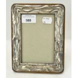 A silver photo frame, cast to simulate bark, mounted on an oak frame,