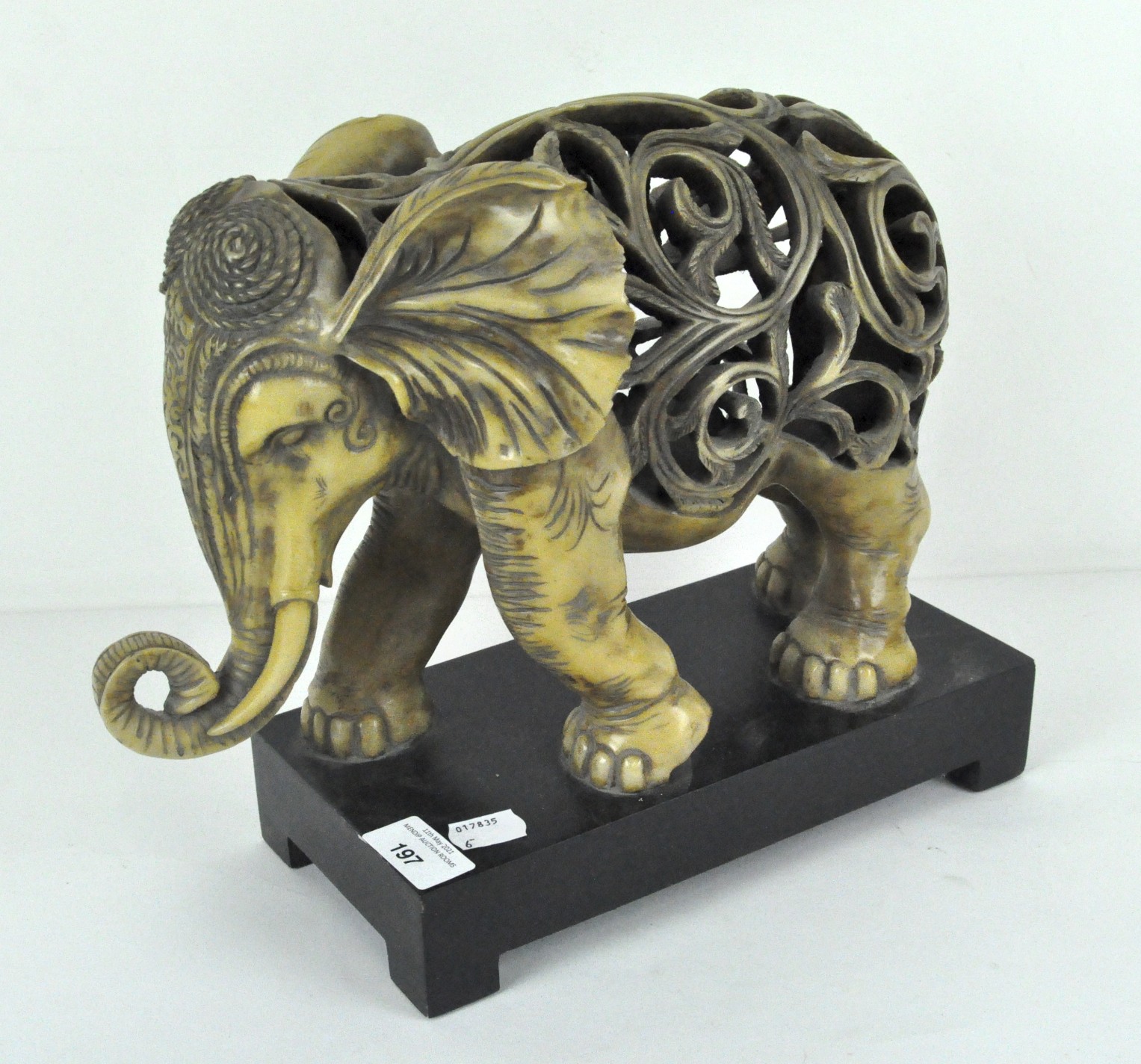 A stylised resin figure of an elephant, raised on wooden stand,