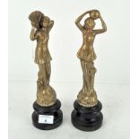 A pair of early 20th century figures of ladies, raised on turned wooden bases,