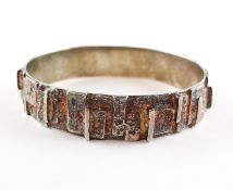A white metal circular bangle of abstract design with textured finish.