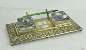 An embossed brass dual inkwell stand with pen rest, two glass inkwells,