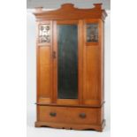 An Art Nouveau oak wardrobe, inset with two foliate copper panels flanking a central mirror,