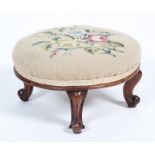 A Victorian walnut low circular footstool, with floral tapestry cover above cabriole legs,