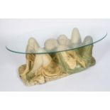 A novelty coffee table, the oval glass top supported on a plaster group of an entwined couple,