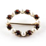 A yellow metal oval brooch set with alternating pearls and garnets. Stamped 9ct