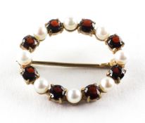 A yellow metal oval brooch set with alternating pearls and garnets. Stamped 9ct