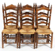 A set of six oak ladder back dining chairs with rush seats, with turned finials,