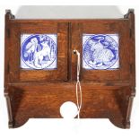 A Victorian oak Gothic Revival hanging wall cupboard mounted with two Minton Aesop's Fables tiles