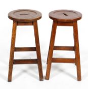 A pair of 20th century oak stools, with recessed circular seats on four chamfered splayed legs,
