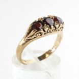 A yellow metal carved half hoop ring set with three round cut garnets.