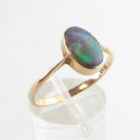 A yellow metal ring set with an oval cabochon cut black opal.