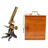 An Edwardian brass microscope in wooden travelling box, with associated fittings and lenses,