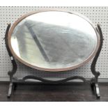 A Regency mahogany swing mirror of oval form, on scroll supports,