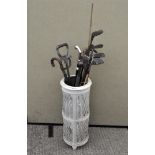 A white painted stick stand containing assorted walking sticks, umbrellas and golf clubs,