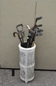 A white painted stick stand containing assorted walking sticks, umbrellas and golf clubs,