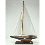 A wooden pond yacht, with fabric sails and string riggings, attached to a rectangular wooden base,