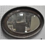 An oval bevelled mirror in a wooden frame with carved details,