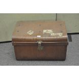A vintage metal trunk, painted brown with brass fittings and stickers to the outside,