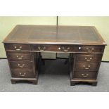 An oak twin pedestal desk with inset brown leather top above nine drawers,