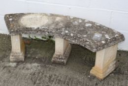 A crescent shaped cast stone garden bench with three supports decorated with florets,
