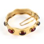 A Victorian gold and garnet set hinged bangle, of wavy form with ten oval cabochons,