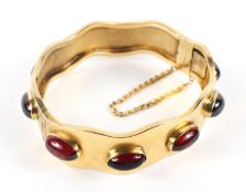 A Victorian gold and garnet set hinged bangle, of wavy form with ten oval cabochons,