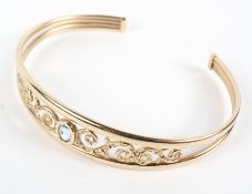 A yellow metal bangle with pierced scroll design and set with an oval 5mm x 4mm blue stone.