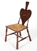 An Arts and Craft chair, the heart shaped back with carved strapwork above a rush seat,