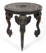 A carved Indian hardwood elephant table, the circular top with scrolling flowers and figures,