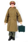 An Action man, with moulded brown hair, wearing a green great coat, jumper, trousers,
