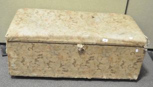 An upholstered ottoman, covered in a faded rose pattern fabric,