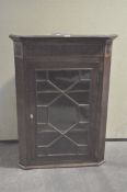 A Georgian mahogany inlaid corner cabinet with two shelves behind a glazed door, with lock and key,