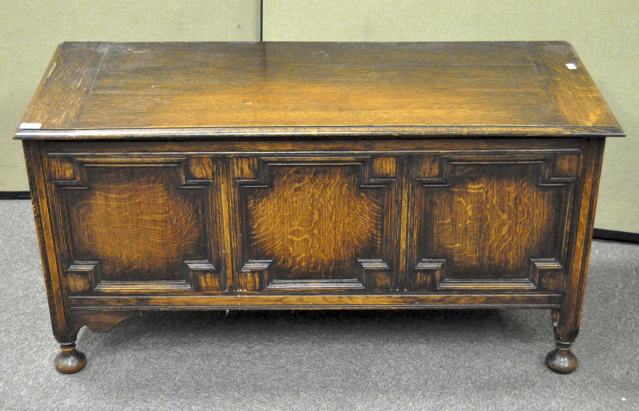 An antique oak coffer with three panel front, the front carved with lozenges, on raised feet,