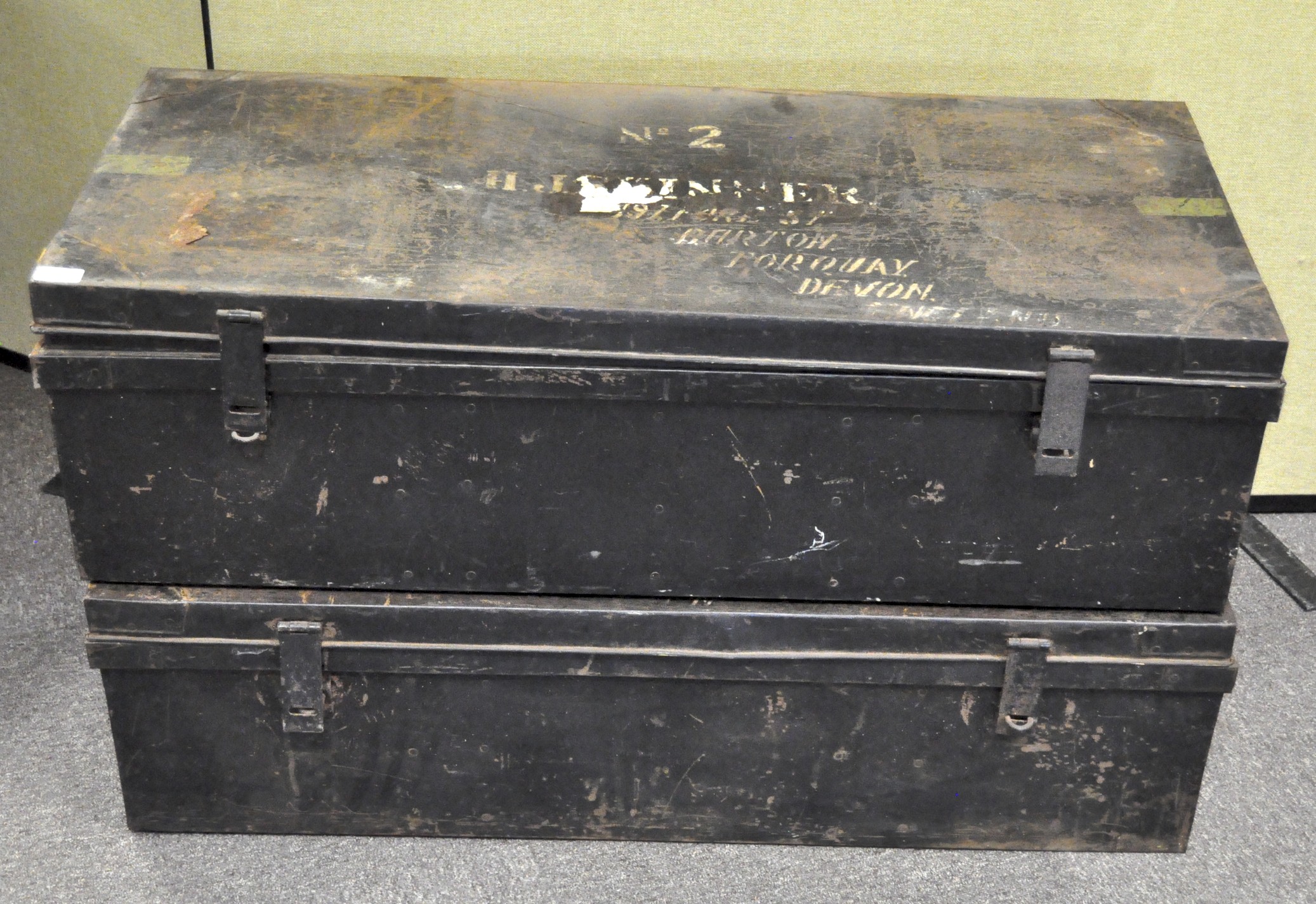 Two large metal trunks, one stamped with a name and address, painted black with hinged lids,