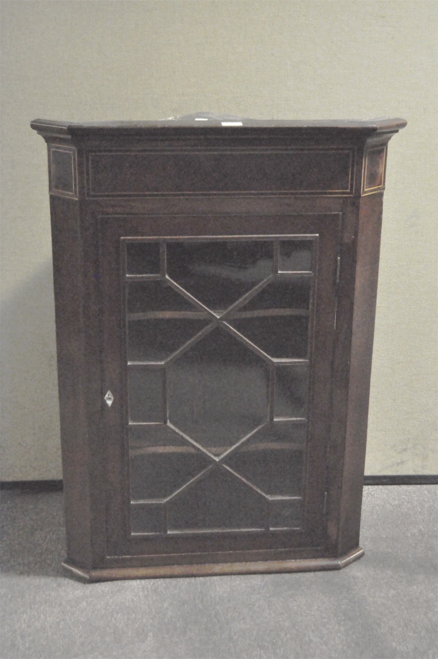 A George III mahogany inlaid corner cabinet with two shelves behind glazed door, with lock and key,