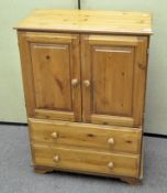 A modern low pine cupboard with two doors above two drawers,