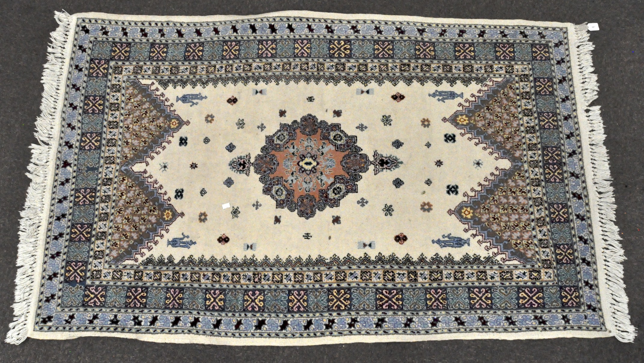 A contemporary rug, featuring a central motif upon a cream ground with blue and red borders,