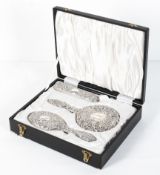 A cased, three piece silver backed dressing table set, with embossed scrolling foliate decoration,