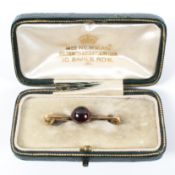 A yellow metal safety pin brooch principally set with a round cabochon cut garnet