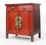 A Chinese red painted hardwood cabinet, with two drawers above two cupboard doors enclosing a shelf,