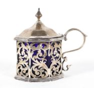 An octagonal silver mustard pot with blue glass liner, pierced with foliate branches,