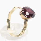 A yellow metal ring set with an oval faceted cut rhodolite garnet