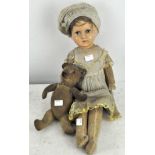 A doll with paper mache head and fabric body in a hat and yellow-trimmed dress,