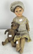 A doll with paper mache head and fabric body in a hat and yellow-trimmed dress,